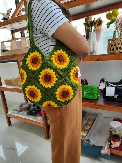 Here is my handmade crochet tote bag with a vibrant sunflower granny square pattern. I used a deep green yarn for the base to make the yellow and brown sunflowers stand out. The bag is shown here being worn to give you an idea of its size and how it hangs from the shoulder.