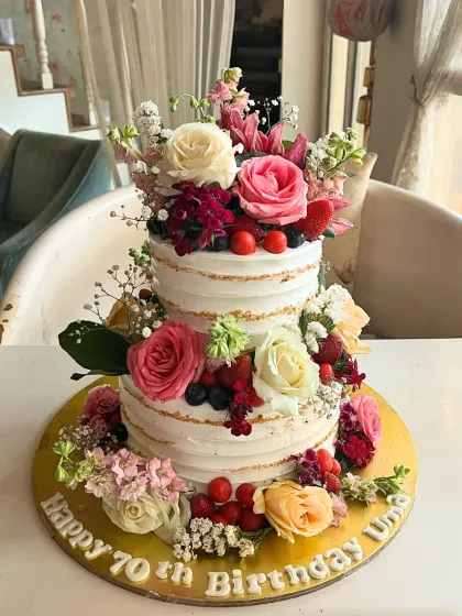 A rustic yet elegant two-tier naked cake, generously decorated with fresh flowers and berries for a 70th birthday.