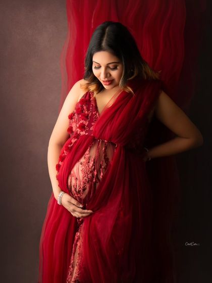 A closer look at the intricate details of this beautiful red gown, featuring delicate floral embroidery over a sheer panel that highlights the baby bump.