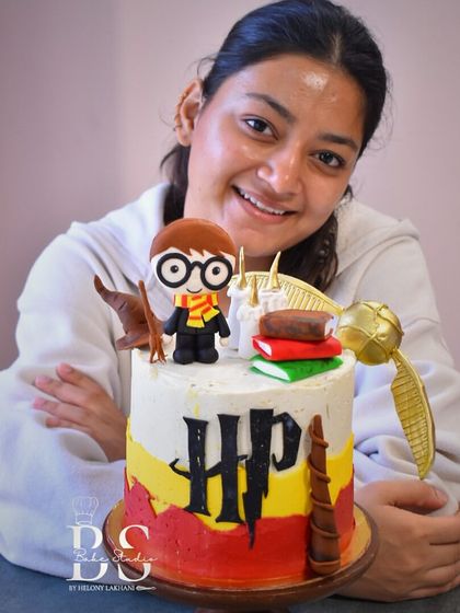 A proud student showcasing her fantastic Harry Potter cake. She learned buttercream coloring techniques, how to apply toppers, and create the iconic "HP" logo.