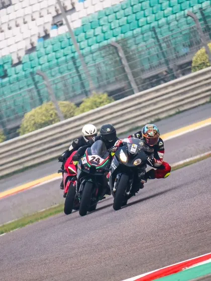A pack of superbikes, led by a rider on a black machine, sweeps through a corner with the grandstands in the background. This is a typical scene from one of our high energy track days.