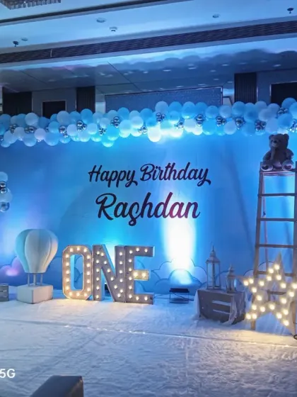 A dreamy blue-themed first birthday for Raghdan. The large stage setup includes a 'ONE' marquee sign, hot air balloon props, and a light-up star for a magical sky theme.