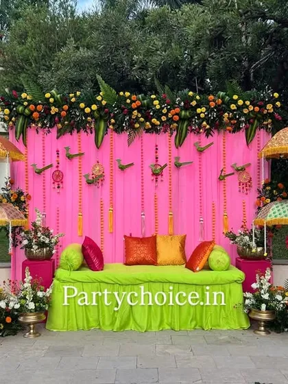 For this outdoor Haldi ceremony, we created a vibrant and festive atmosphere. The setup features a bright pink backdrop, a comfortable lime-green seating area, and decorative Rajasthani umbrellas, all framed by a thick garland of marigolds.
