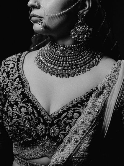 A close-up, black and white shot focusing on the intricate embroidery of the bride's blouse and her stunning necklace.