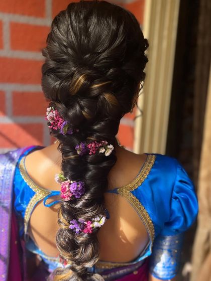 A beautiful, thick braid adorned with a mix of purple and pink flowers. The highlights in the hair add dimension to the style, making the braid look even more intricate and textured.