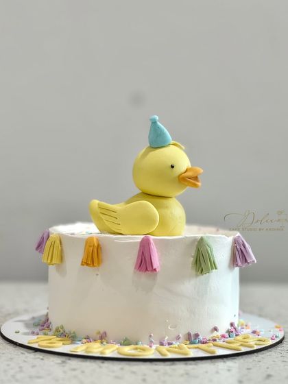 A simple and sweet half-kg duckling cake. The little fondant duck is wearing a party hat and is surrounded by a colorful tassel garland.