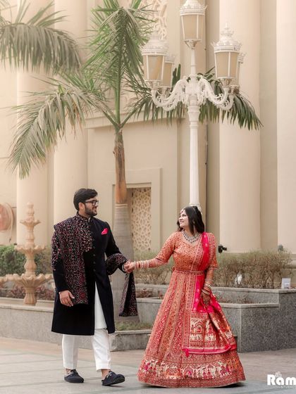 A classic shot of the couple walking hand-in-hand through a grand venue. The groom's embroidered sherwani and the bride's flowing lehenga create a picture of traditional elegance.