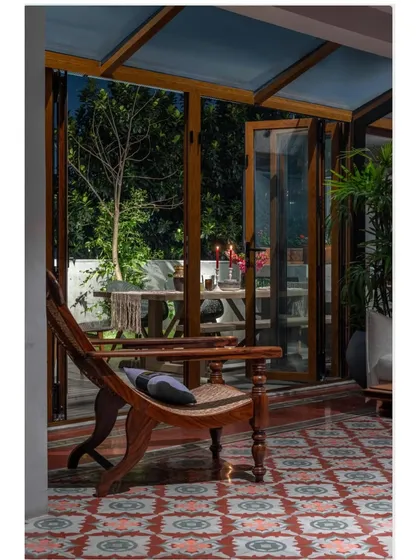 As evening falls, this corner of the Dhaka home transforms. The glass-enclosed seating area looks out onto the garden, creating a serene space to unwind. The easy chair, with its classic design, invites you to sit and watch the day turn to night.