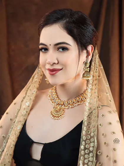 A smiling portrait that captures the beauty of fusion styling. The model wears a modern black top with a traditional necklace and a sheer, embellished dupatta.