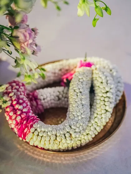 A close-up of the Varmaala, intricately woven with jasmine and pink flowers, ready for the ceremony. The craftsmanship of the garland itself is a key part of the wedding's aesthetic.