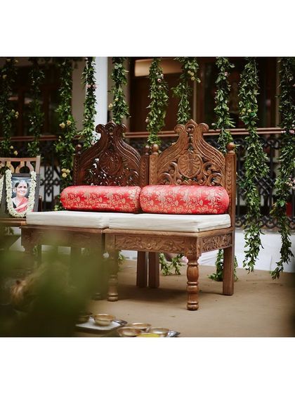 The seating for the couple, featuring intricately carved wooden chairs with bright red cushions for a pop of color.