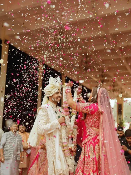 A joyful and dynamic wedding moment capturing the bride and groom during the Varmala ceremony amidst a shower of flower petals. This candid shot freezes a moment of pure celebration and happiness.