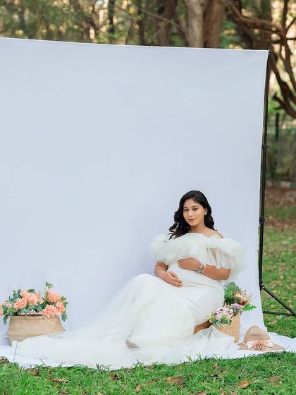 A serene, seated portrait capturing the peaceful moments of pregnancy. The flowing white gown spreads out beautifully on the grass, creating an angelic look.