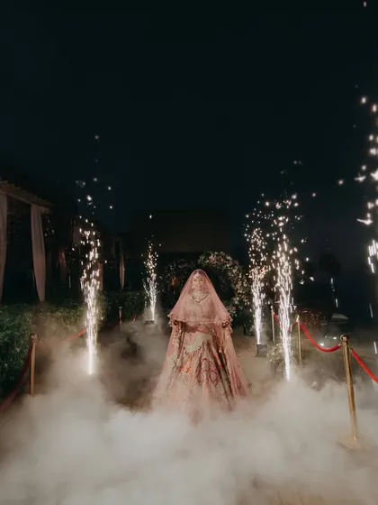 A powerful shot of Radhika's entrance, shrouded in smoke and flanked by pyrotechnics. This image captures the grandeur and excitement of a modern bridal entry.