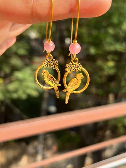 These sweet gold-tone earrings feature a parrot sitting in a hoop, accented with a pink bead. They are lightweight and perfect for daily wear.