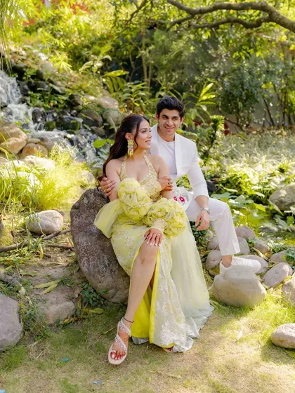 A classic couple portrait set in a lush, green garden with a waterfall. Their coordinated designer outfits in yellow and white add a touch of sunshine to this serene and romantic pre-wedding picture.