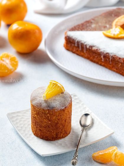 A mini orange drizzle cake with a dusting of powdered sugar, styled with fresh oranges for a bright and zesty product shot.