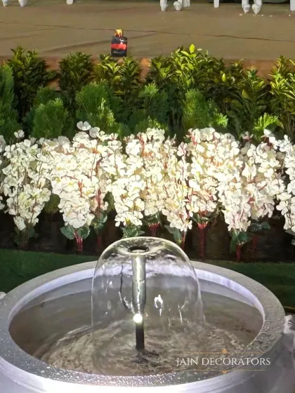 The soothing sound of water adds another sensory layer to the decor. This small fountain is surrounded by white blossoms, creating a tranquil and beautiful focal point in the garden.