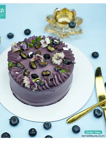 A top-down view of the Blueberry Cake, showing the arrangement of fresh blueberries and edible flowers across the top.
