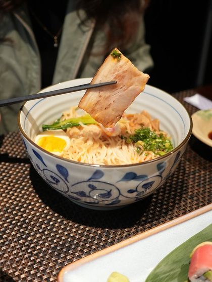 A guest enjoying a bowl of our Ebisu Ramen, showcasing a piece of the tender chashu pork. It's a complete and balanced meal in a single bowl.