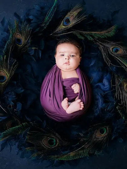 Our newborn photography is all about capturing delicate details. Here, a peacefully swaddled baby is nestled in a wreath of peacock feathers, creating a unique and artistic portrait.