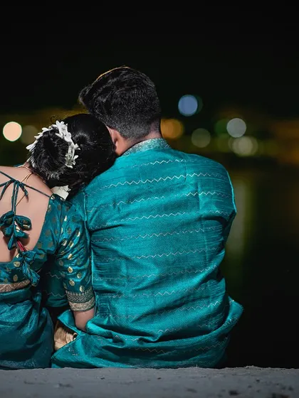 A quiet moment of peace, sitting by the ghats with the reflection of the city lights on the Ganga. The bride rests her head on his shoulder, a simple gesture of comfort and love.