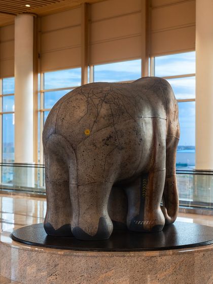 A rear view of Arunkumar H. G.'s elephant sculpture 'Impinged II' at the airport, showing the intricate surface details and the beautiful backdrop of the airfield.
