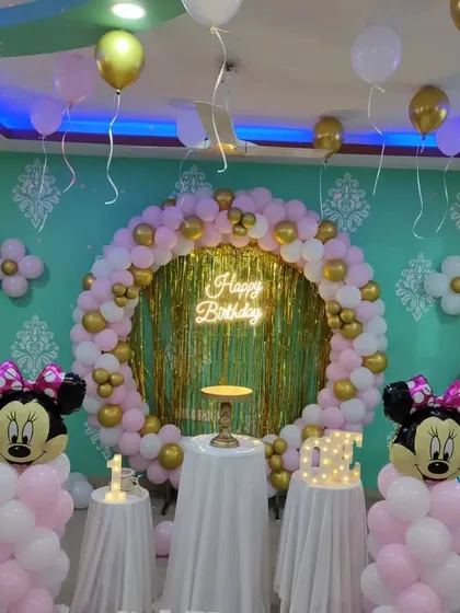 A Minnie Mouse theme with a circular balloon arch and a gold tinsel backdrop. The pink, white, and gold color scheme creates a sweet and celebratory look.