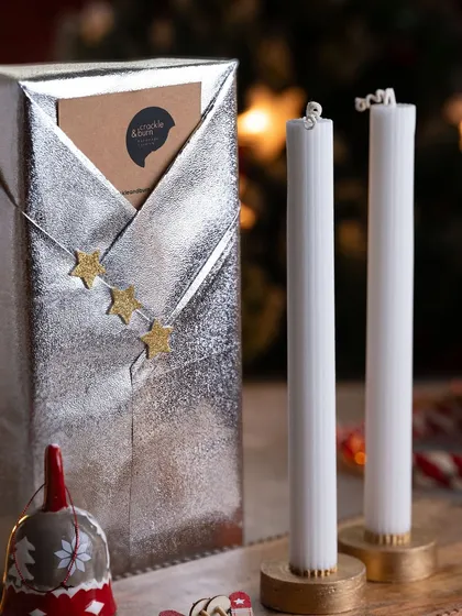 Elegance personified. A gift wrapped in shimmering silver paper next to two of my classic white tapered candles in simple gold holders.