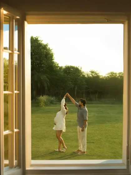 A fairytale moment. Framed by an open window, the couple shares a dance on a lush green lawn, creating a romantic, cinematic scene that feels like a dream.