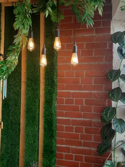 A cozy balcony corner can be created with the right textures and lighting. Here, I used a brick-patterned wall, artificial grass panels, and warm Edison bulbs to make a beautiful and inviting space.