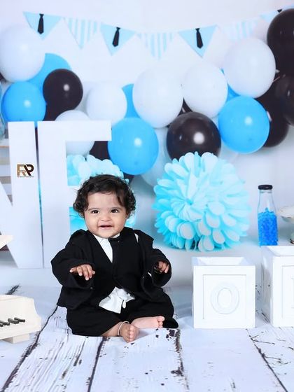 A baby boy dressed as a "Boss Baby" sits confidently in a chair, surrounded by blue, black, and white decorations. This stylish and fun theme is full of personality.