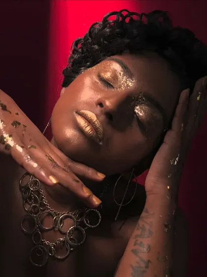A powerful editorial portrait with a focus on texture, from the glossy, glittery eyes to the gold leaf accents.