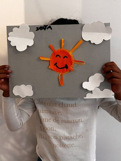 "Shine bright like the sun." A student hides behind their happy sun craft, made with looped paper for extra dimension.