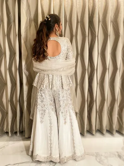The full look of the client with her stone-accessorized ponytail, wearing a stunning white and silver sharara set.