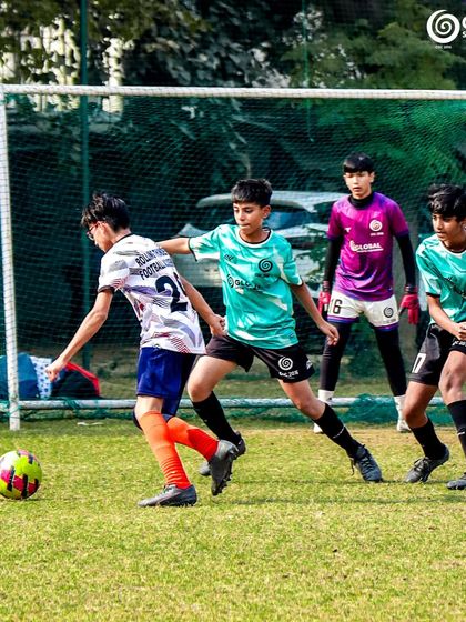 An attacking player moves the ball towards the goal as defenders and the goalkeeper prepare to defend.