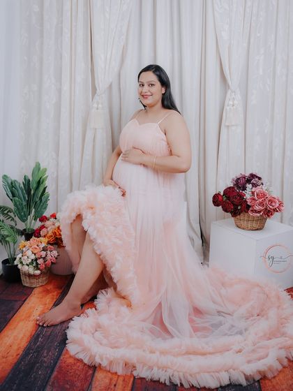 A gorgeous mom-to-be seated in a soft pink ruffled gown. The rustic wood floor and floral props create a warm and charming studio setting.