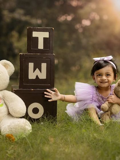 A happy moment with her furry friends in the park. The warm sunlight adds a magical glow to this second birthday photo.