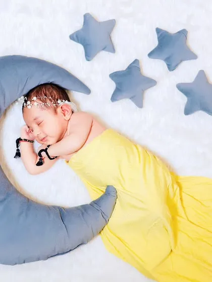 A full-length view of the newborn in a yellow swaddle on the moon prop, creating a beautiful and imaginative scene.