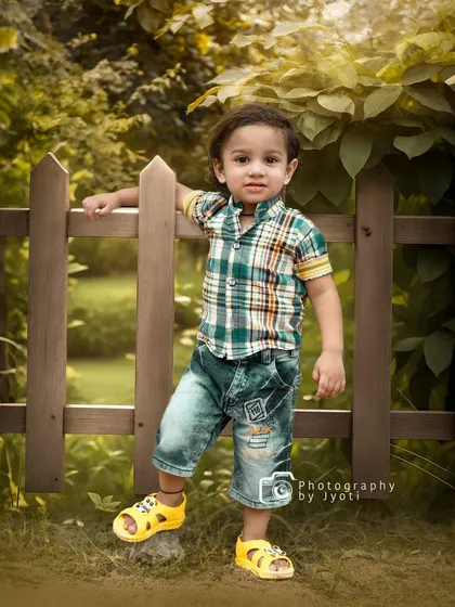 A confident pose from a little boy during his outdoor photoshoot, leaning against a wooden fence in a park. I aim to capture the unique personality of every child.