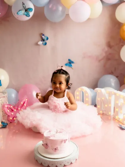A wider view of a complete cake smash setup. This butterfly theme includes a custom backdrop, a balloon arch in pastel colors, and light up letters spelling 'ONE' to create a dreamy, celebratory atmosphere.