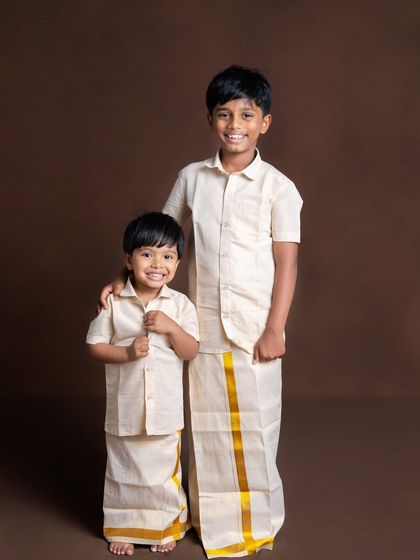 Two brothers in matching traditional veshtis, sharing a happy moment. This classic studio portrait captures their bond and their shared heritage.