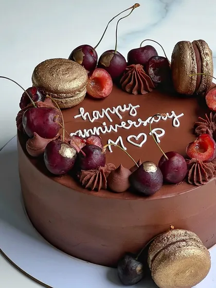 A beautiful chocolate anniversary cake topped with fresh cherries and gold-dusted macarons. The combination of rich chocolate and tart fruit is always a winner.