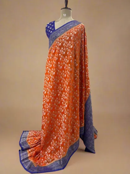 A vibrant orange soft crepe saree with a white floral jaal and a contrasting blue border.