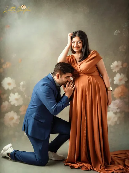 A dramatic and elegant studio maternity portrait. The combination of the flowing gown and the painted floral backdrop creates a stunning, artistic effect.