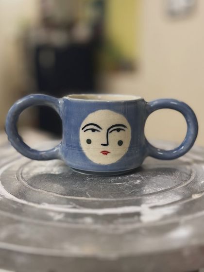 A quirky little mug with two handles and a serene face, created by Deepica. It’s a playful piece that shows her unique creative voice.