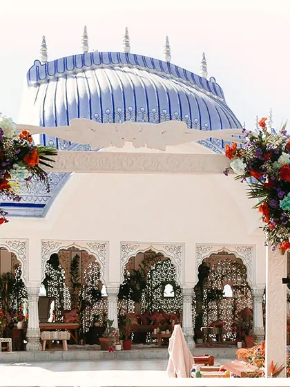 A grand view of the Mehendi setup at The Leela Palace, with the iconic blue-domed roof in the background. The decor is designed to complement the venue's magnificent architecture.