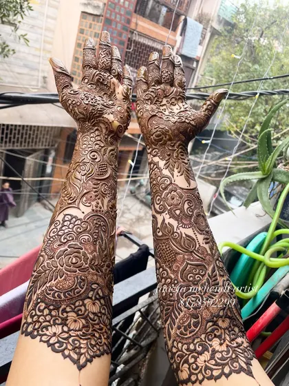 A full-length view of a bridal mehendi design, held up against the sky. The intricate patterns cover the hands and arms completely.