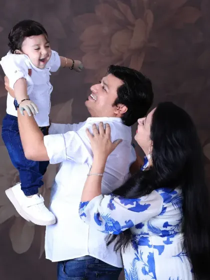 A dynamic and joyful family photo. The father lifts his laughing baby high in the air as the mother looks on with a smile, capturing a perfect moment of candid happiness.