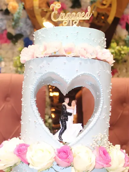This shot highlights the "Engaged" topper and the delicate floral work on the top tiers of the custom blue engagement cake. Every detail is crafted to match the celebratory theme.